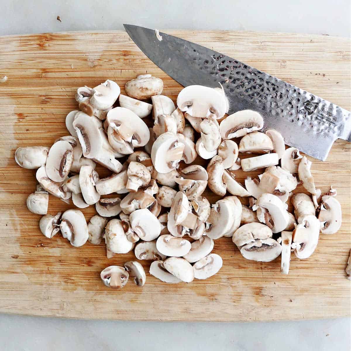 white button mushrooms sliced on a cutting board with a knife