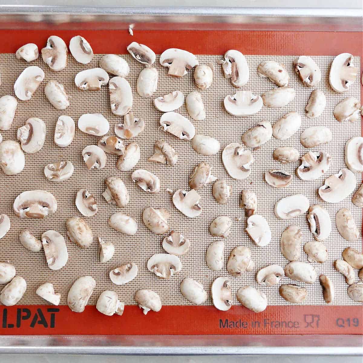 sliced mushrooms spread out on a lined baking sheet to be frozen