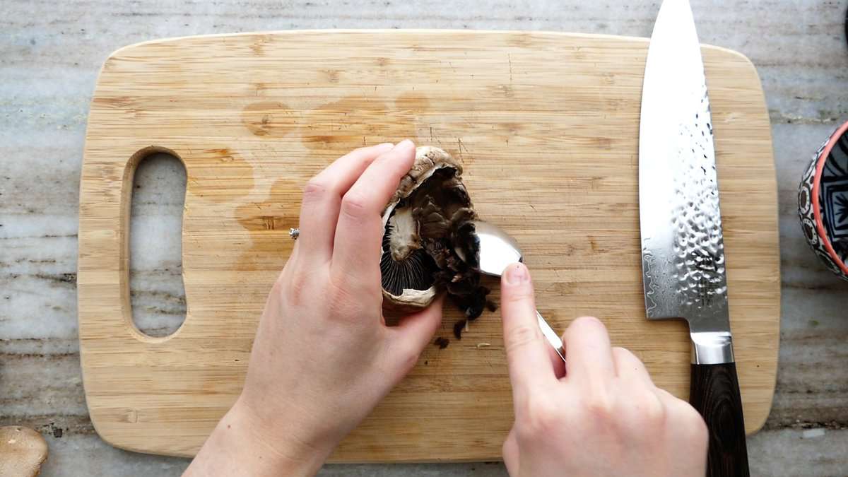 woman cleaning out the gills of a portobello mushroom