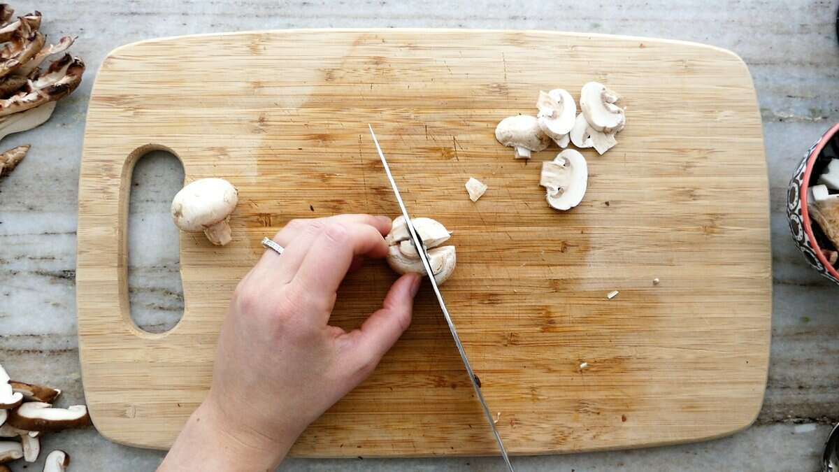 woman cutting a white mushroom into quarters on a cutting board