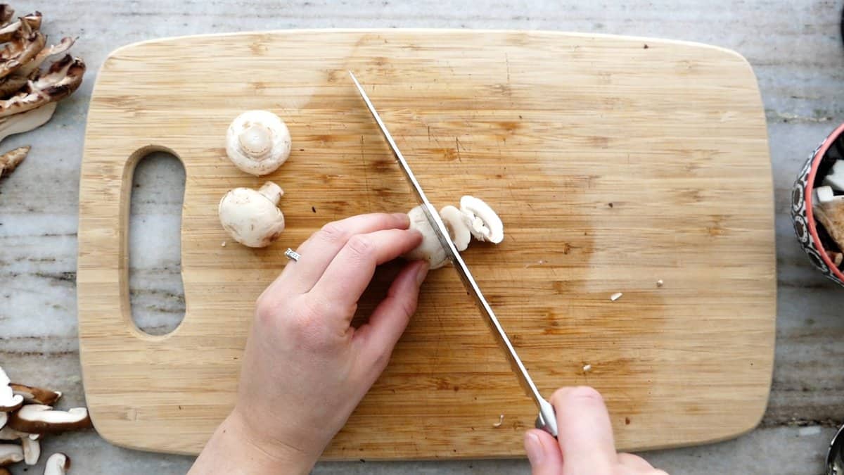 woman cutting a button mushroom into slices on a cutting board
