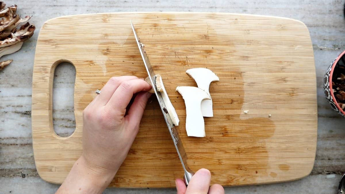 woman cutting a king trumpet mushroom on a cutting board