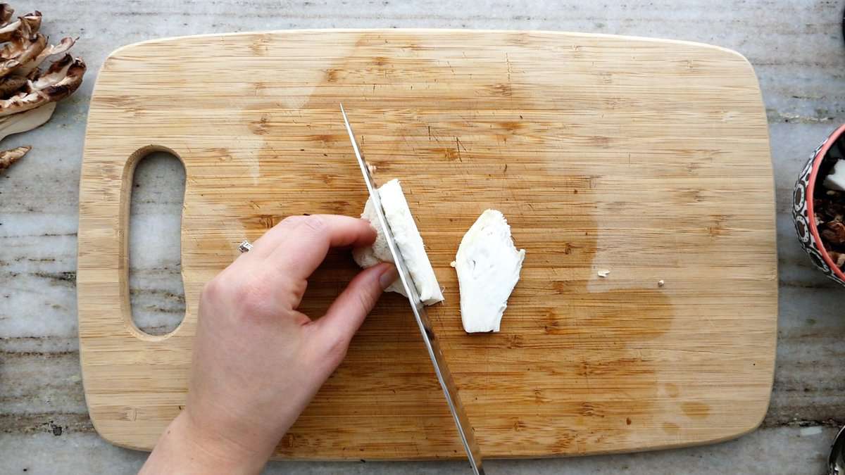 woman cutting a lion's mane mushroom on a cutting board