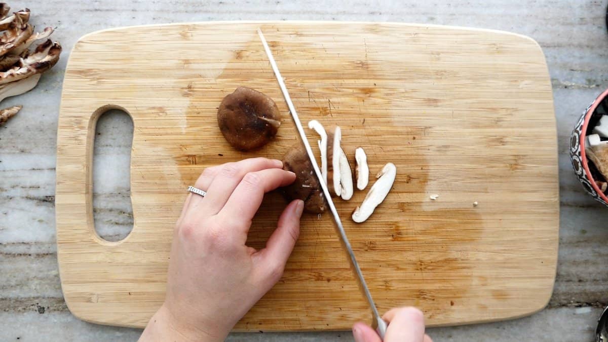woman slicing a shiitake mushroom on a cutting board