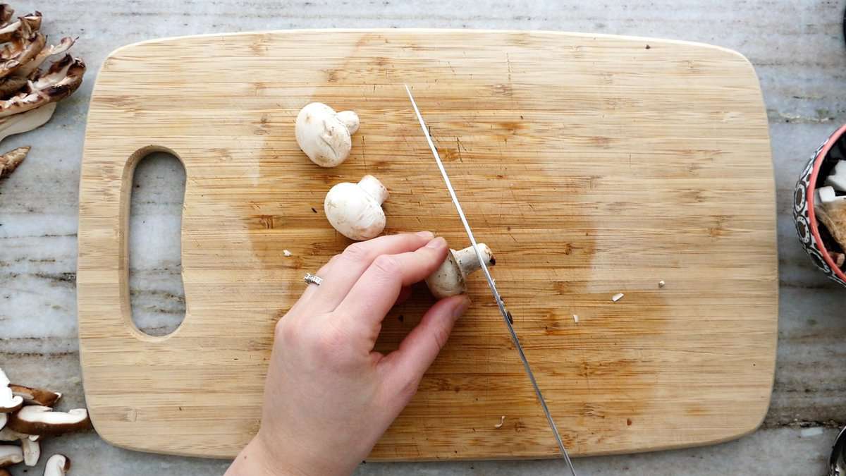 woman trimming a button mushroom on a cutting board