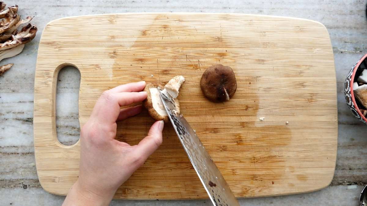 woman trimming a shiitake mushroom on a cutting board