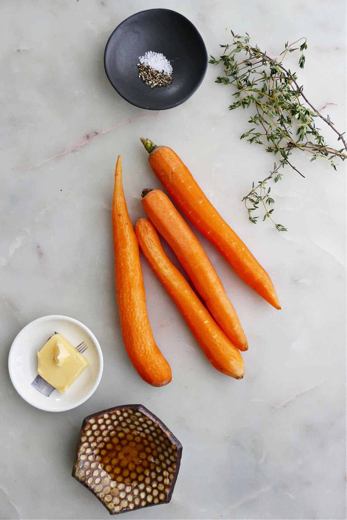 carrots, thyme, salt, pepper, honey, and butter on a counter