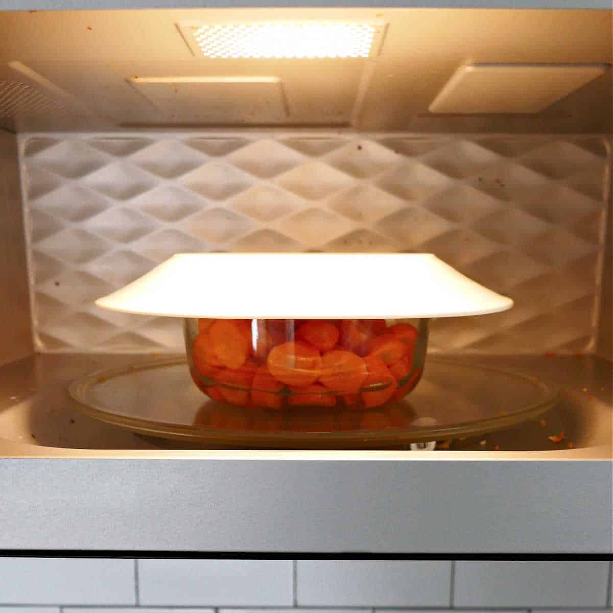 carrots in a bowl with a plate on top in the microwave