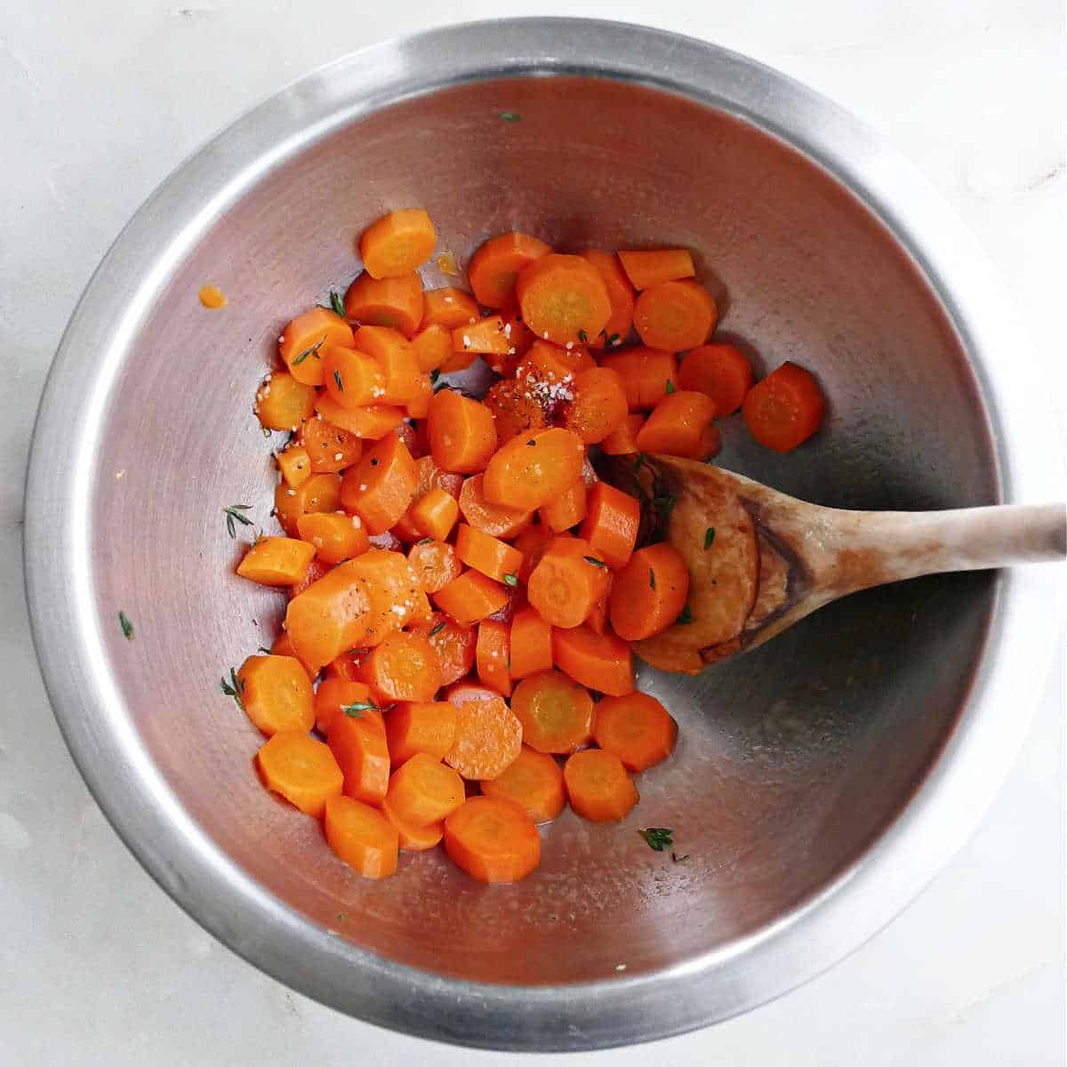 cooked carrots with seasonings in a mixing bowl with a spoon