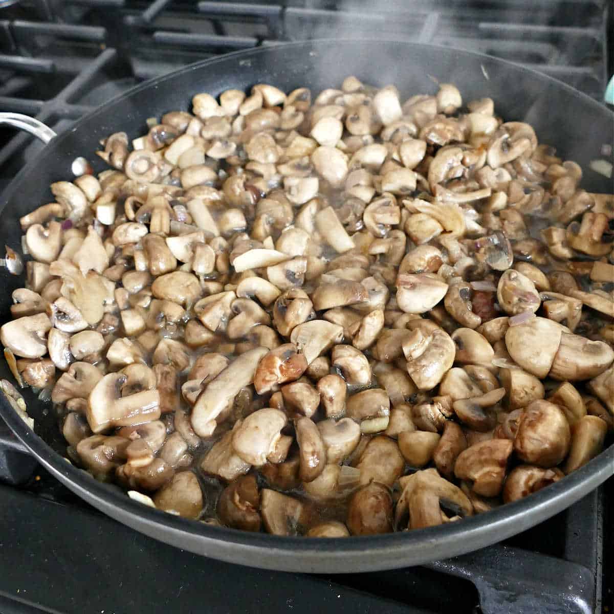 mushrooms cooking down in a skillet on a stove