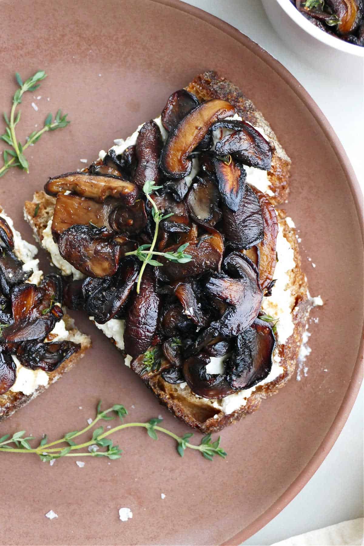 slice of mushroom ricotta toast with thyme sprigs on a serving plate