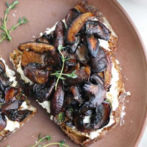 slice of mushroom ricotta toast with thyme sprigs on a serving plate