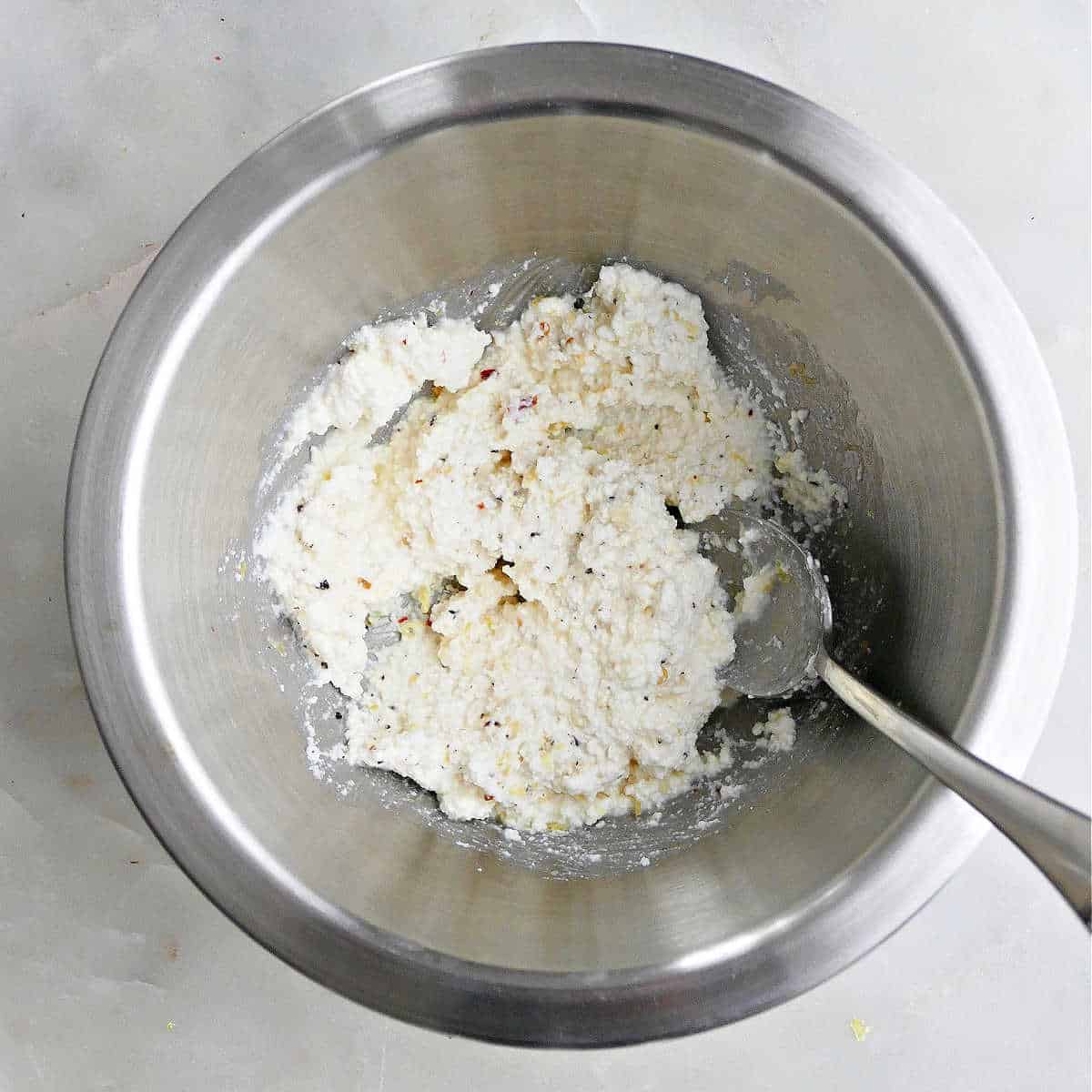 ricotta cheese being mixed with seasonings in a bowl on a counter