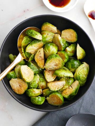 steamed Brussels sprouts in a serving bowl next to toppings