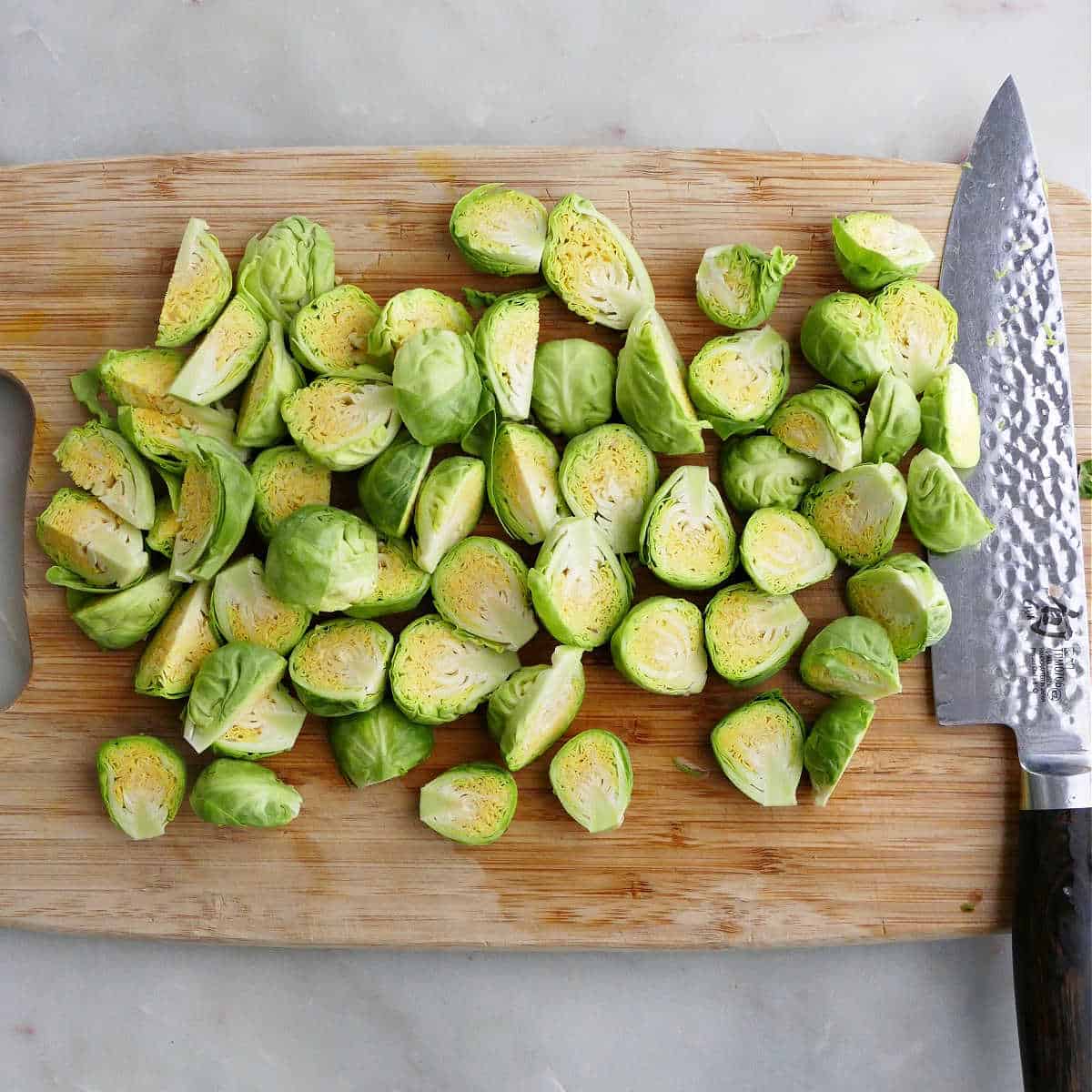 Brussels sprouts sliced in half on a cutting board with a knife