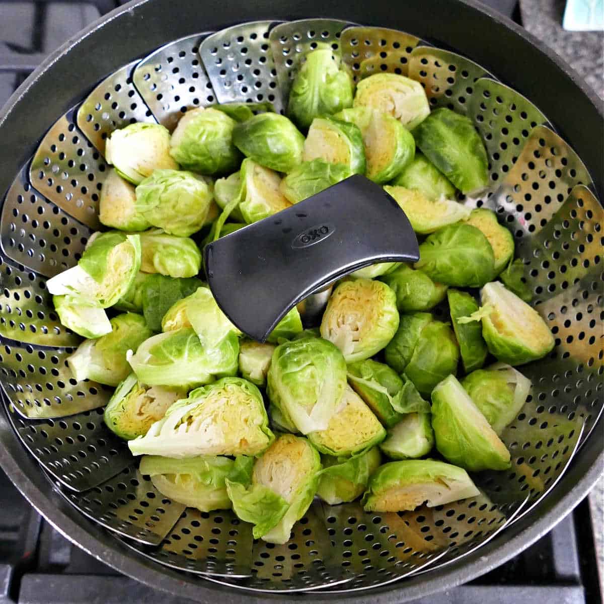 sliced Brussels sprouts cooking in a steamer basket in a large pot