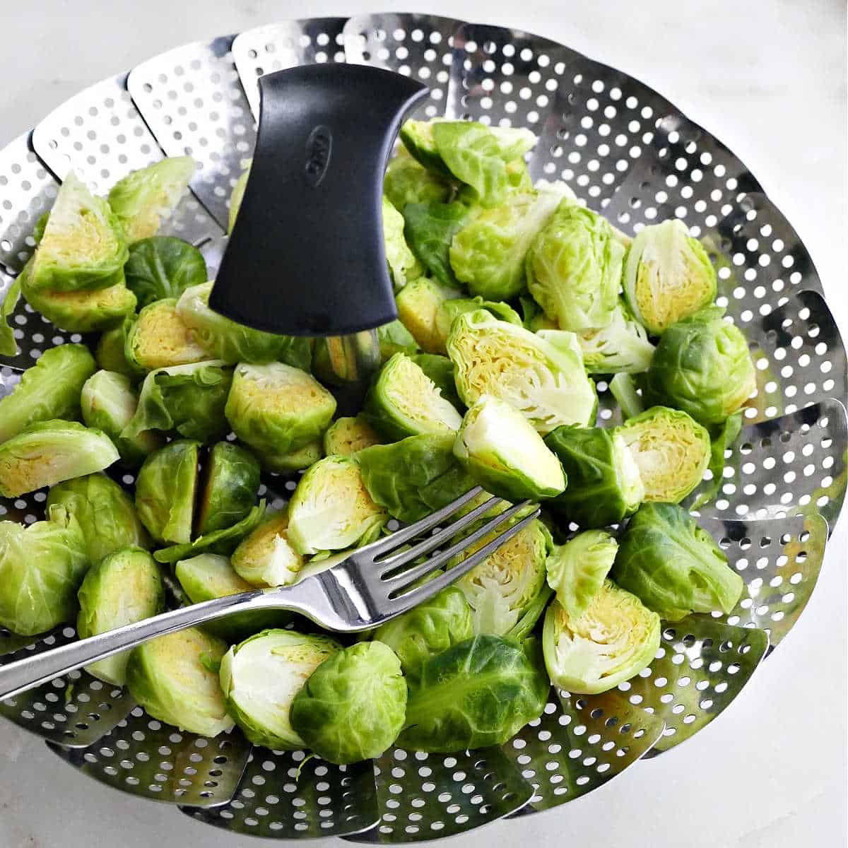steamed Brussels sprouts in a steamer basket with a fork