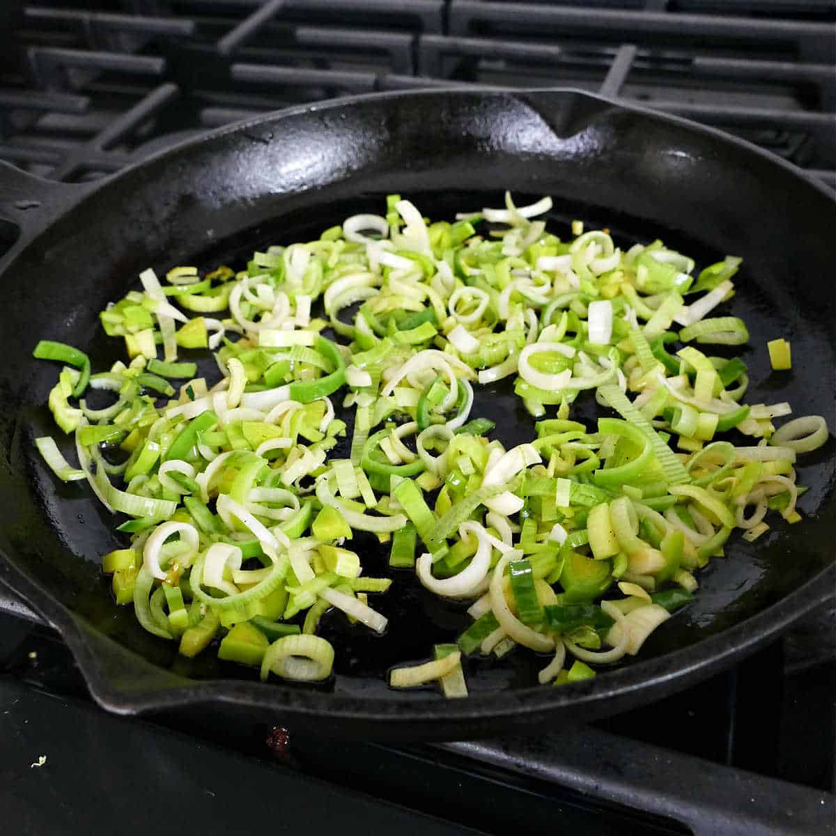 chopped leeks cooking in olive oil in a cast iron skillet