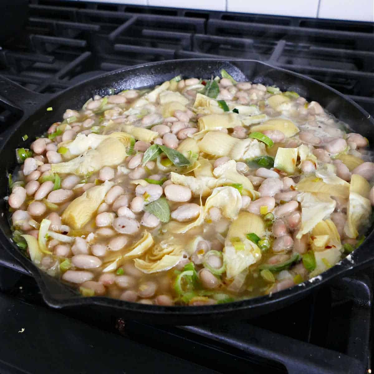 white beans, artichokes, leeks, and broth simmering in a skillet