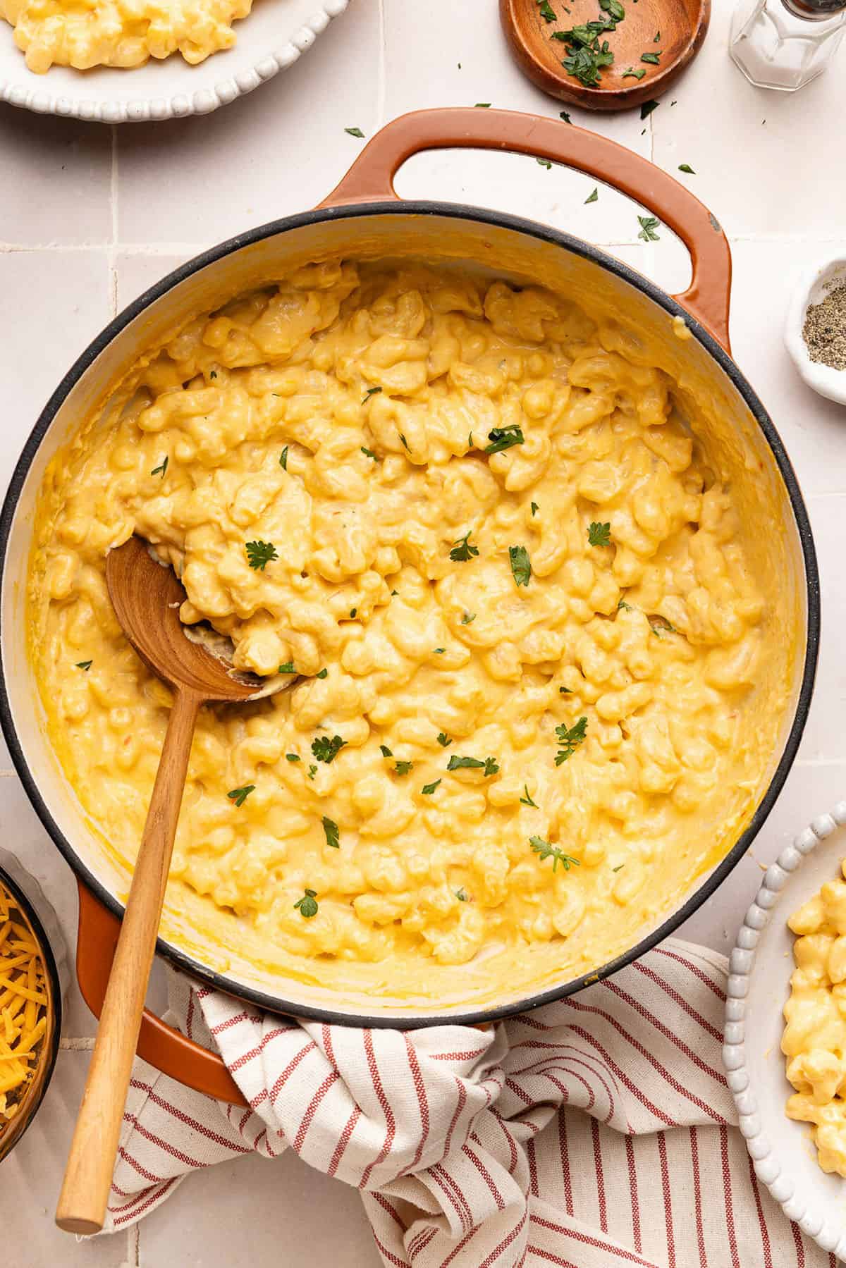 Creamy veggie mac and cheese in a pot with a wooden spoon surrounded by ingredients.
