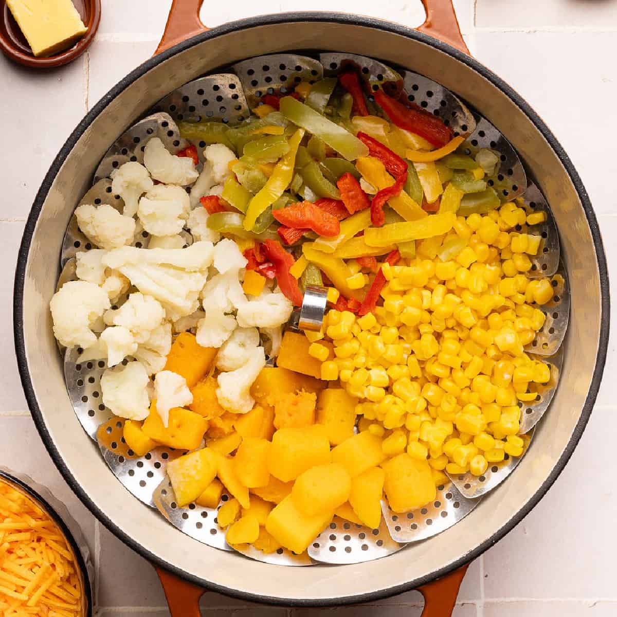 Cauliflower, bell peppers, corn, and squash steaming in a basket in a pot.