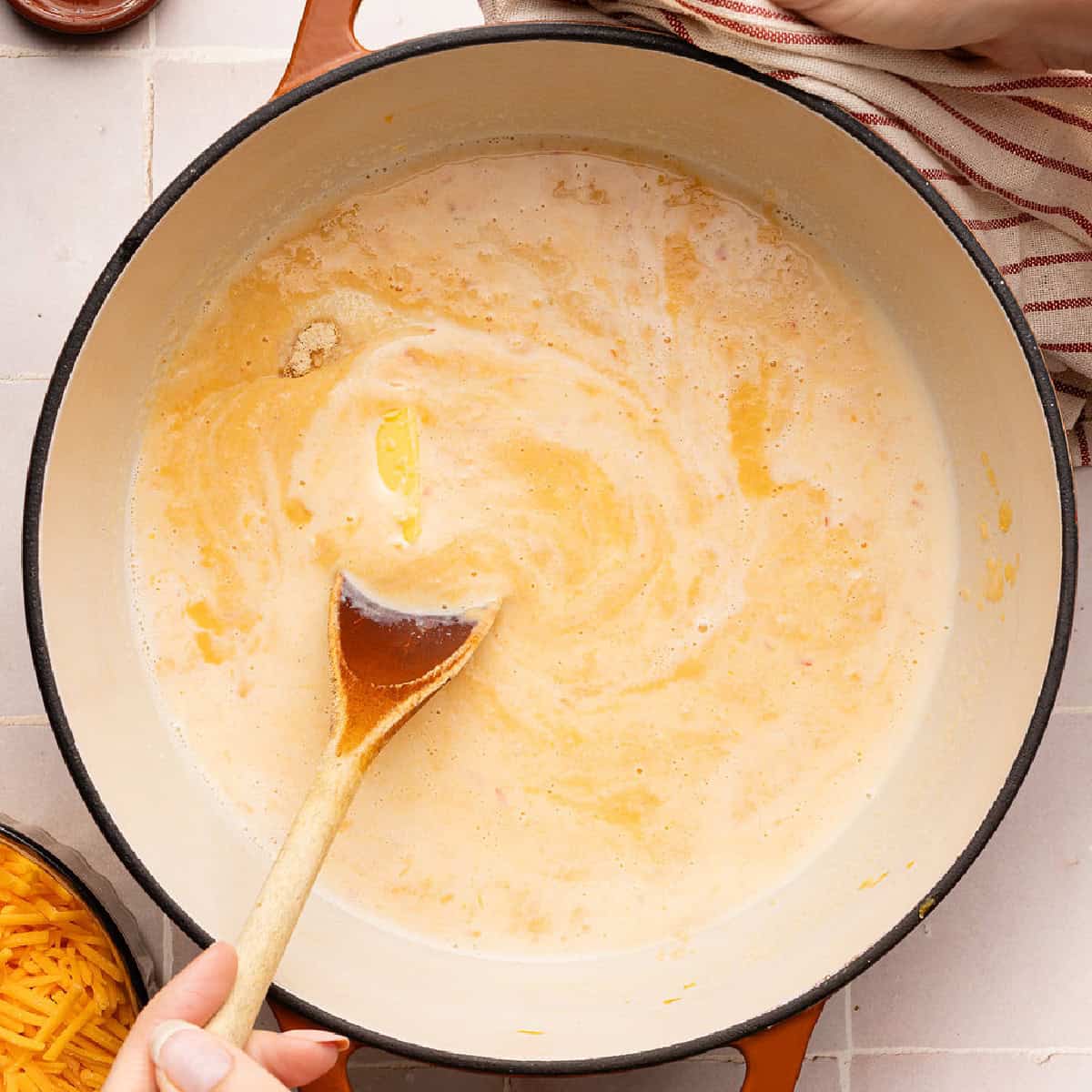 Woman stirring veggie and milk sauce with butter in a large pot.