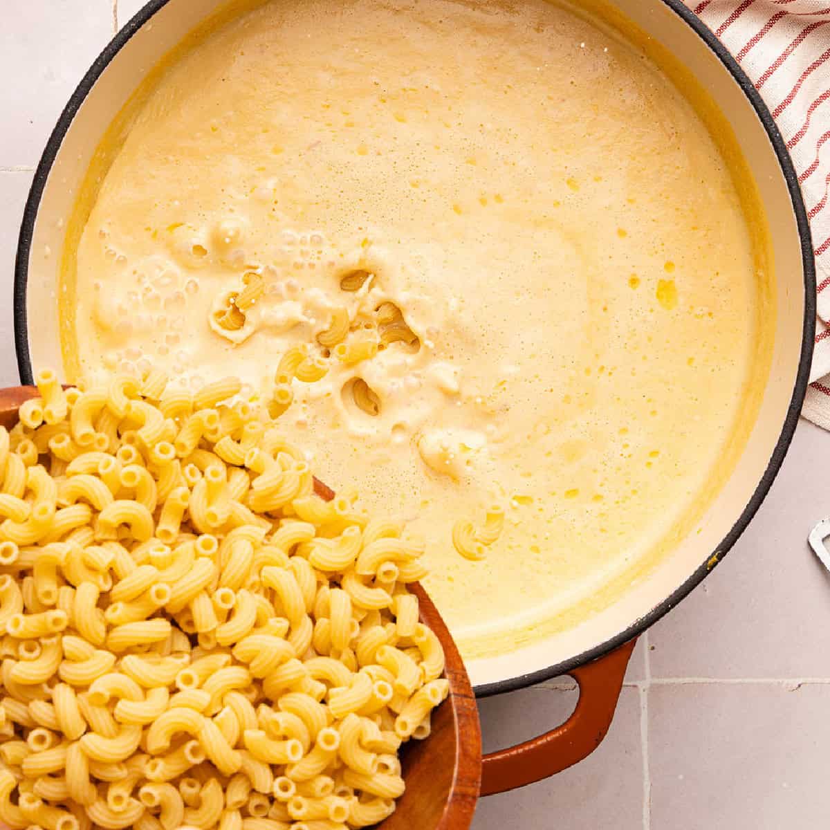 Woman pouring elbow macaroni into orange sauce made from veggies and milk in a pot.