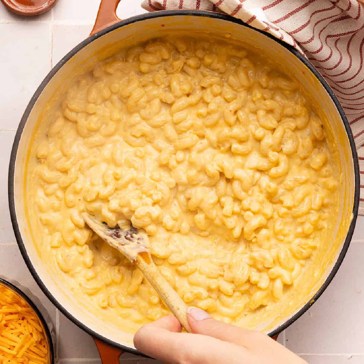 Woman stirring veggie mac and cheese with a wooden spoon in a large pot.