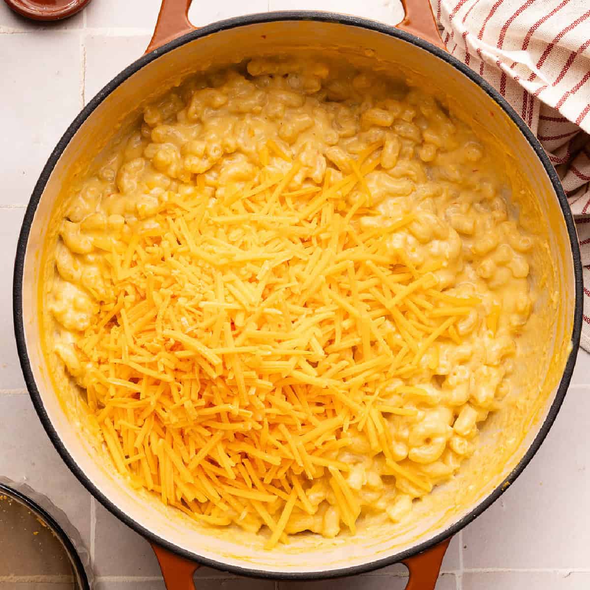 Shredded cheddar cheese added to a pot of macaroni coated in vegetable sauce.