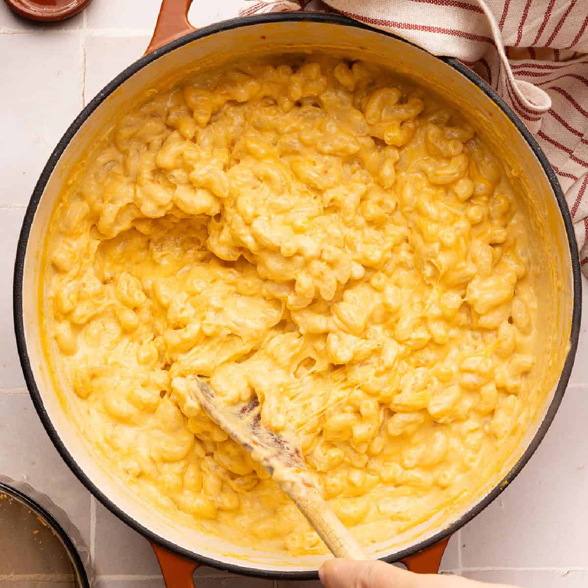 Woman stirring orange hidden veggie mac and cheese in a large pot.