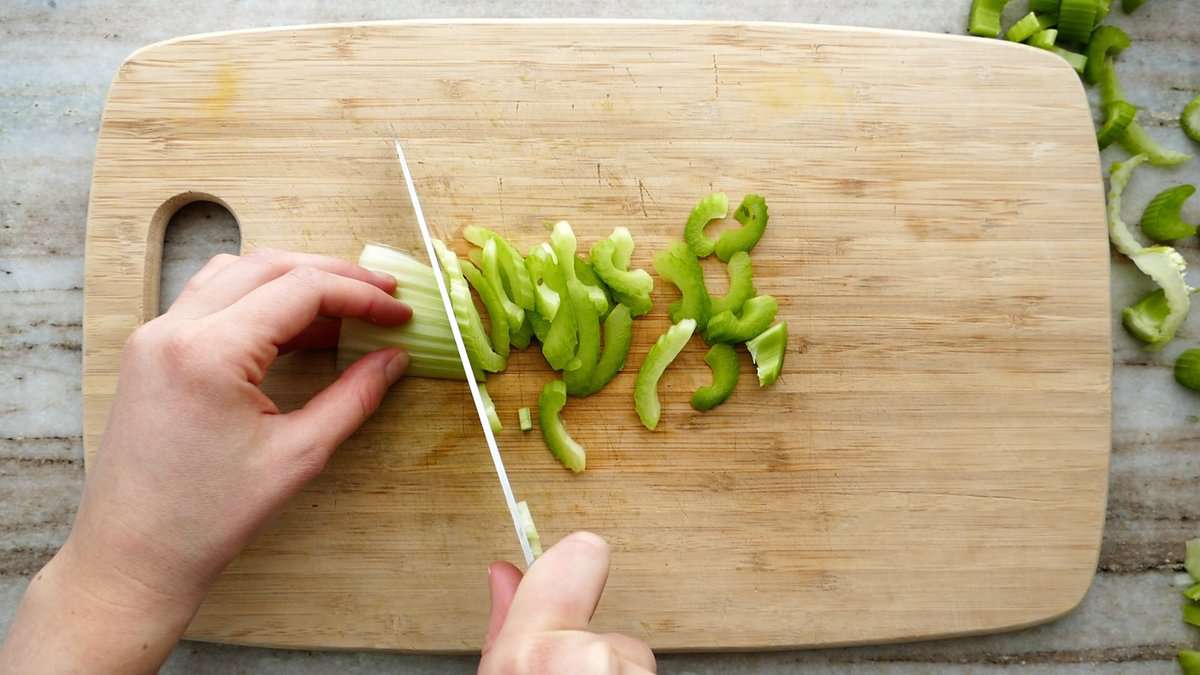 woman slicing celery on an angle on a cutting board