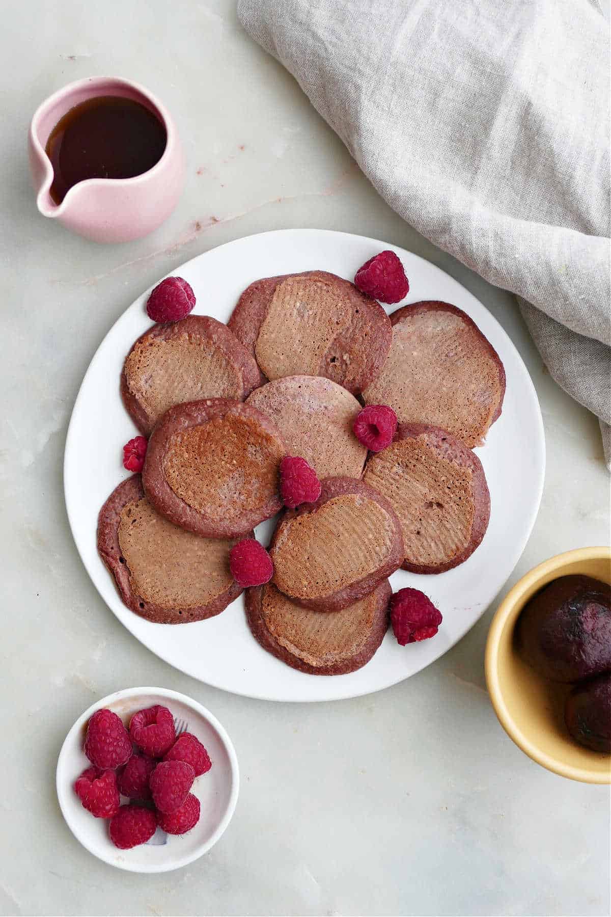 beet pancakes on a plate with raspberries next to toppings on a counter