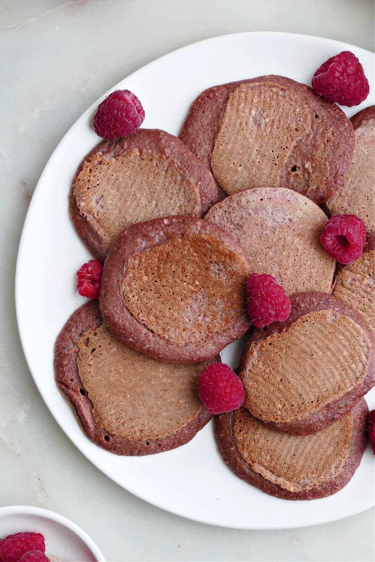 beet pancakes on a plate with raspberries on top