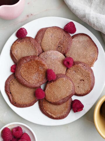 beet pancakes on a plate with raspberries next to toppings on a counter
