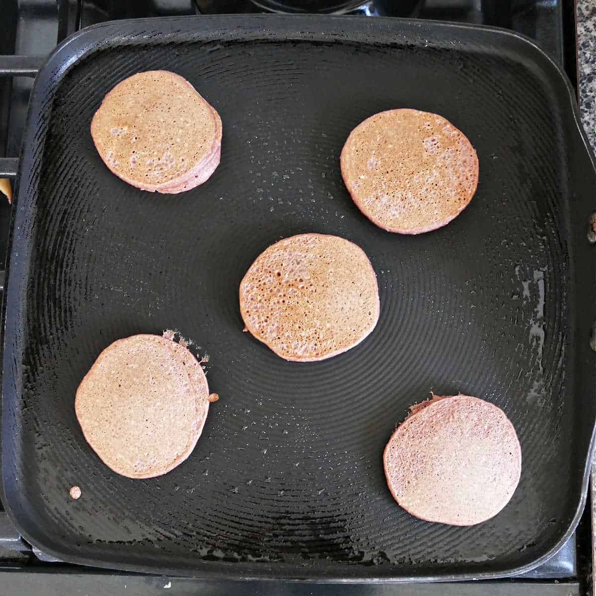 five small beet pancakes cooking in coconut oil on a griddle