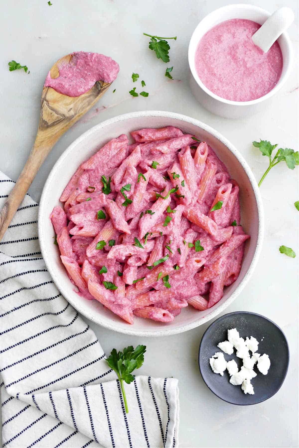 beet pasta in a serving bowl next to toppings and a napkin