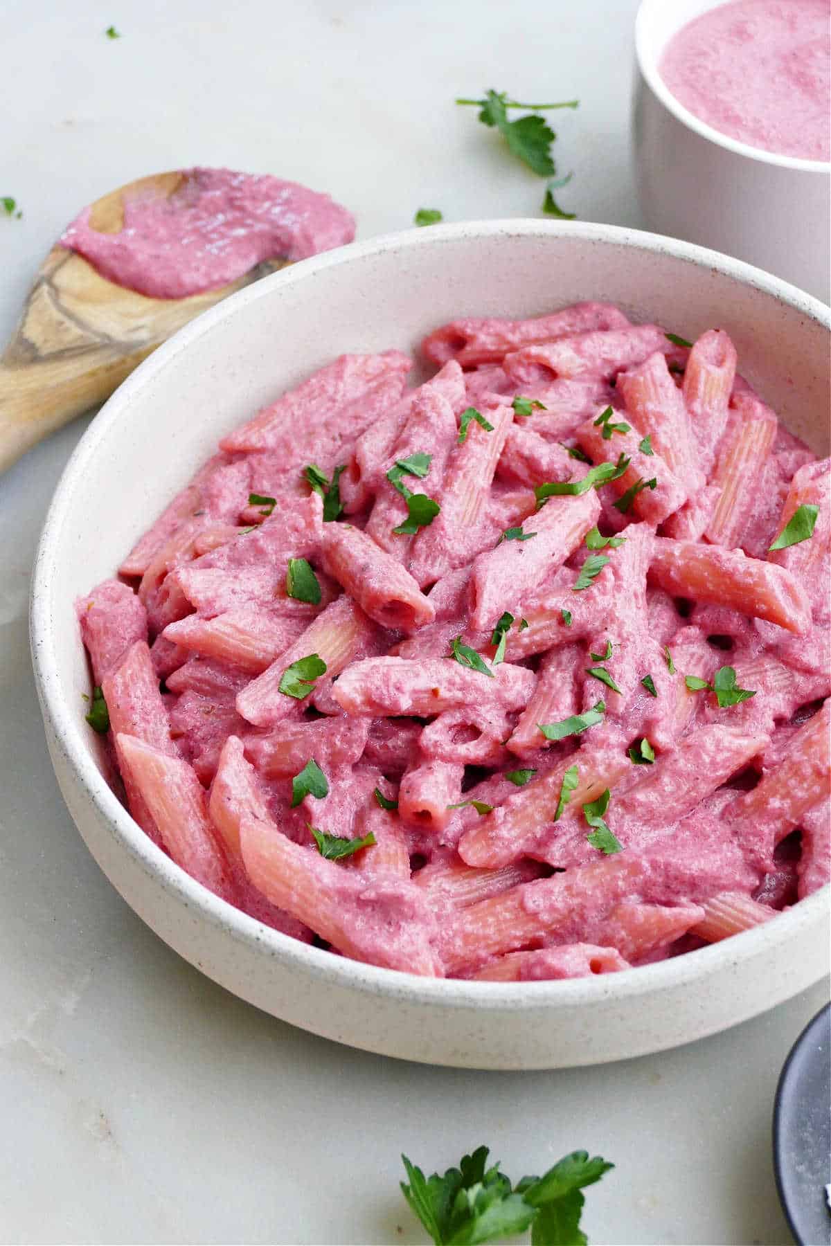 pasta tossed with blended beet sauce in a bowl topped with parsley