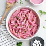 beet pasta in a serving bowl next to toppings and a napkin