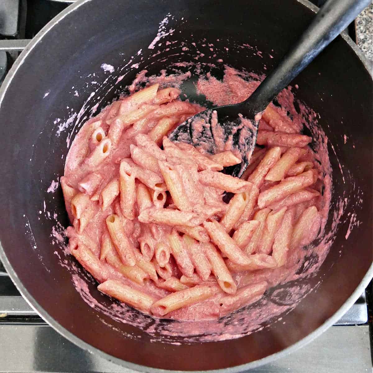 pasta tossed with beet sauce in a pot with a spoon
