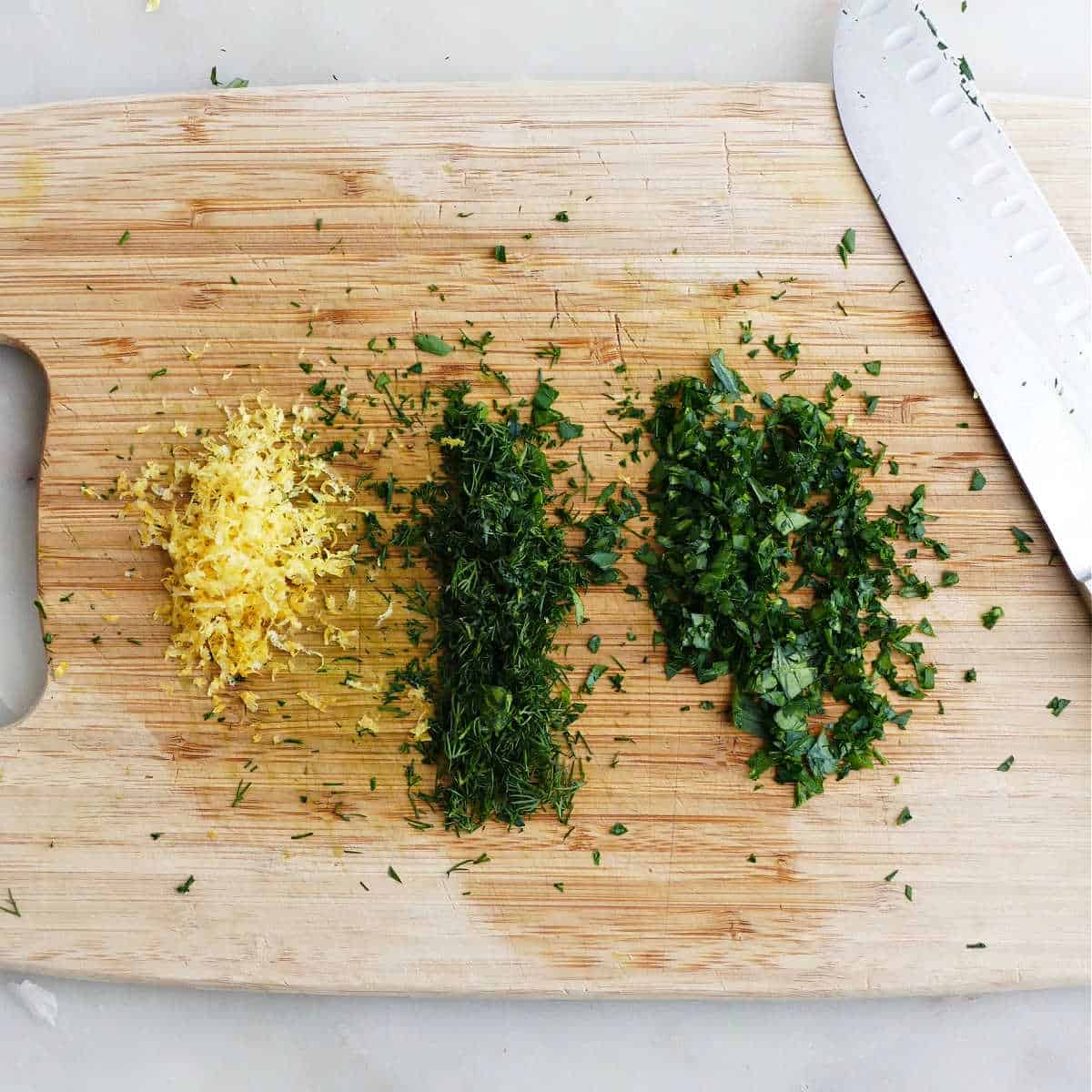 lemon zest next to chopped dill and parsley on a cutting board