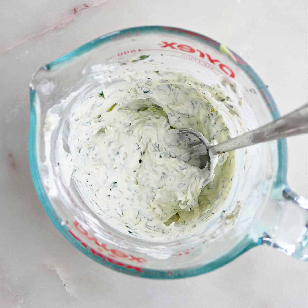 mascarpone cheese being mixed together with garlic, herbs, and lemon in a measuring cup