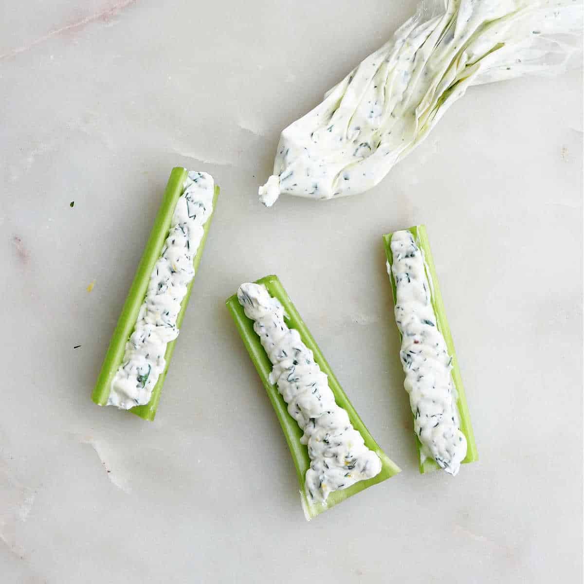 mascarpone cheese being piped into celery sticks on a counter