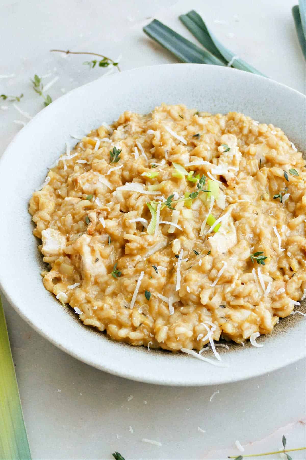 chicken and leek risotto topped with thyme and parmesan cheese in a bowl
