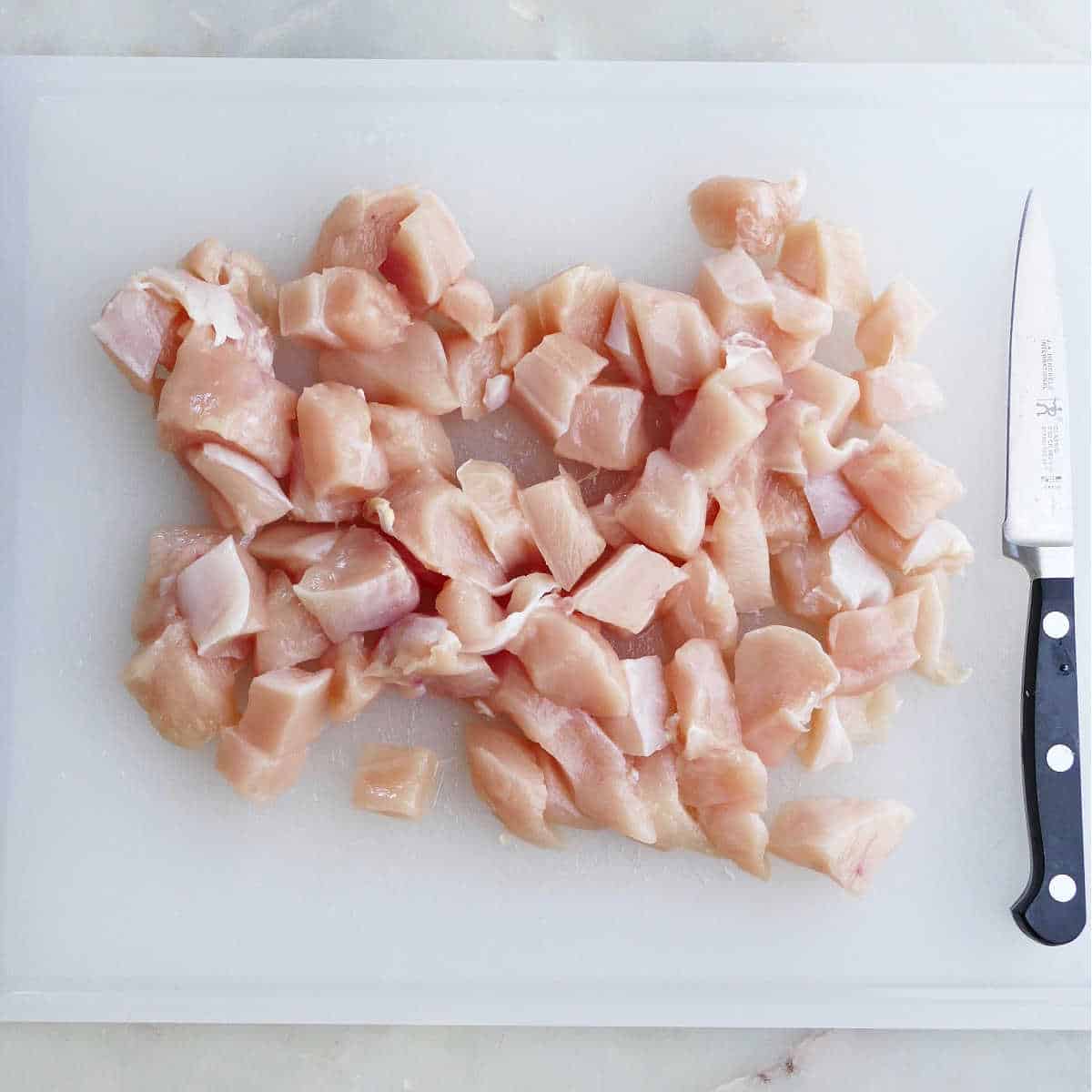 chicken breast cut into cubes on a cutting board with knife