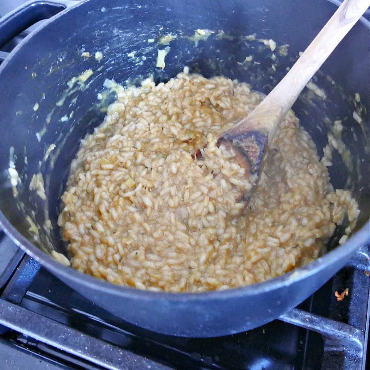 chicken leek risotto cooking in a soup pot being stirred with a spoon