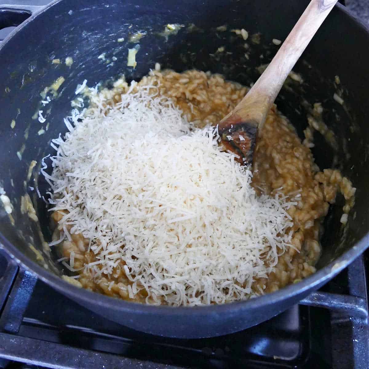 parmesan cheese being stirred into risotto in a soup pot