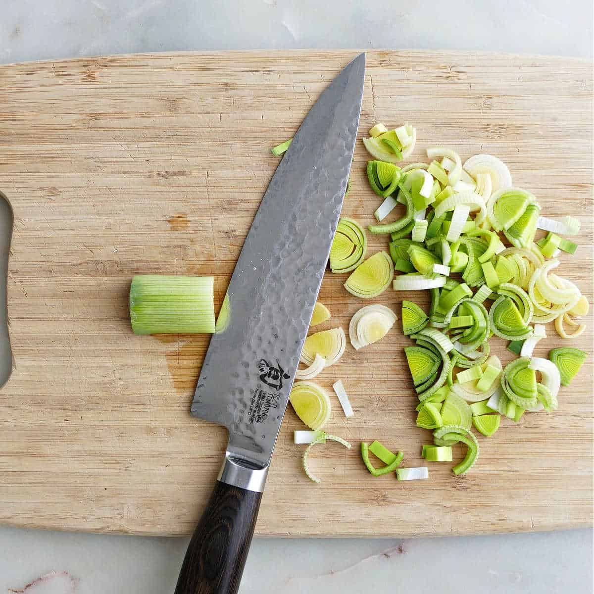 leeks being cut into half-moon pieces on a cutting board