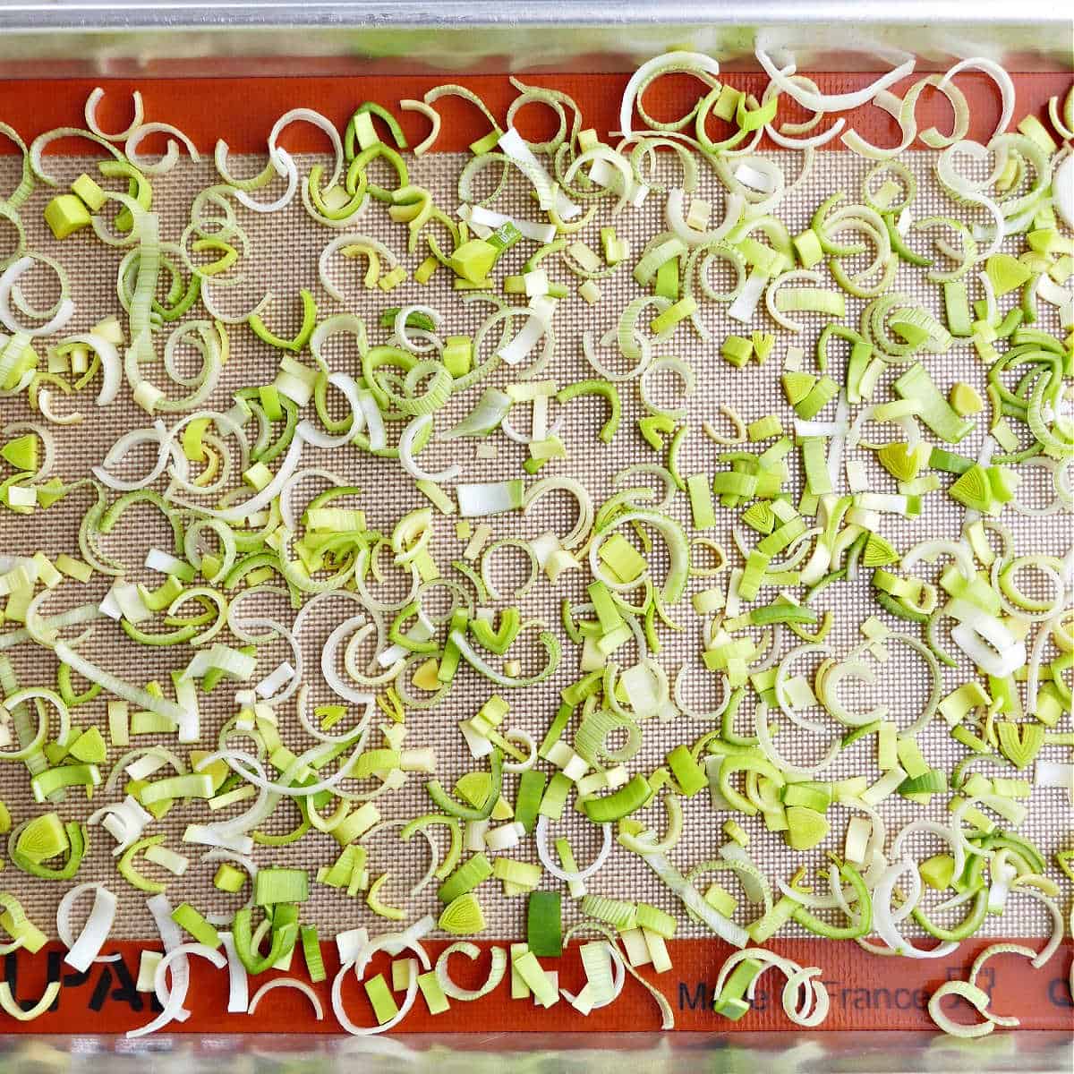 cut leeks spread out on a lined baking sheet before being frozen