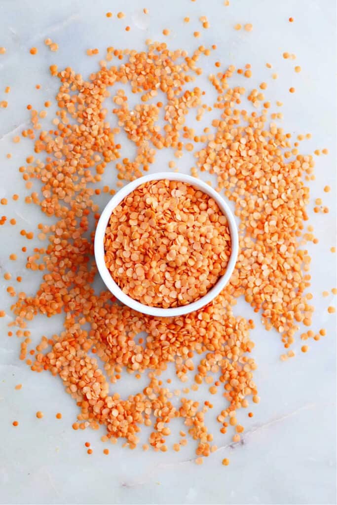 dry red split lentils in a bowl surrounded by loose lentils on a counter