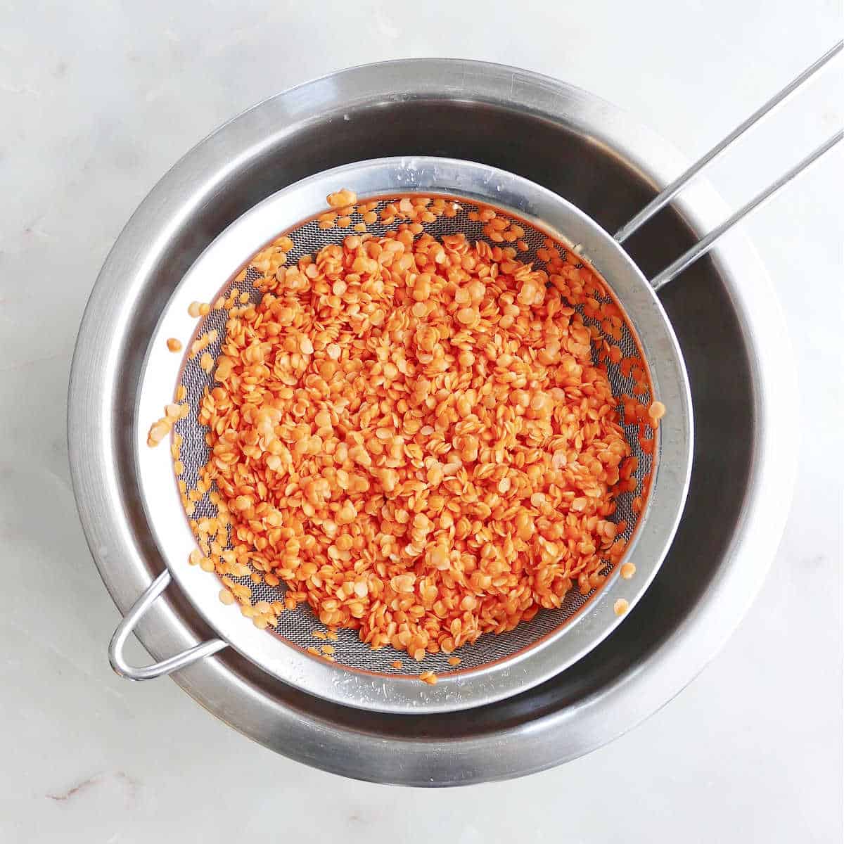 red split lentils draining after being rinsed over a bowl on a counter